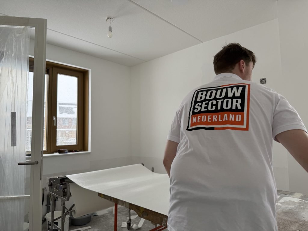 Behanger van Bouwsector Nederland bij de plaktafel met een baan renovlies in een lege kamer
