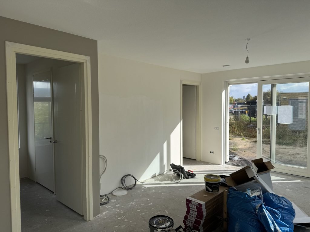 Nieuwbouwwoonkamer tijdens de afwerking, met lichte wanden en materiaal op de vloer