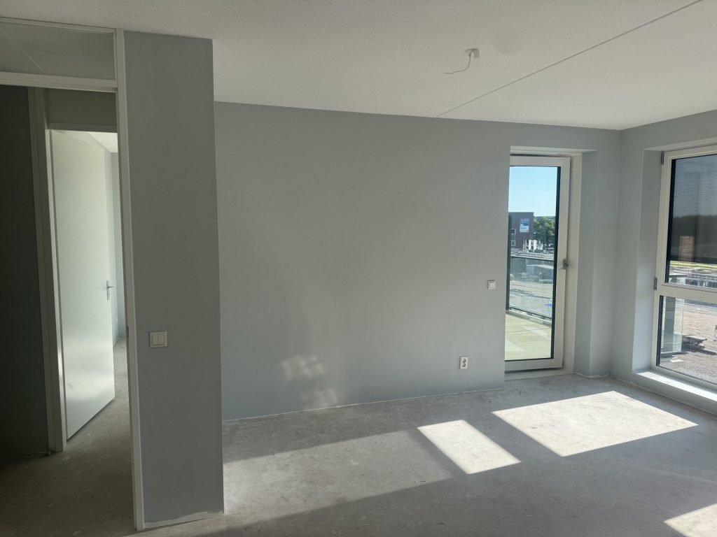Lege nieuwbouwkamer met lichtgrijze wanden en zonlicht op de betonvloer