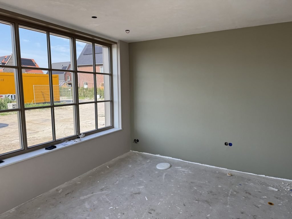 Nieuwbouwkamer met een egaal gesausde wand in een grijsgroene tint naast een groot raam