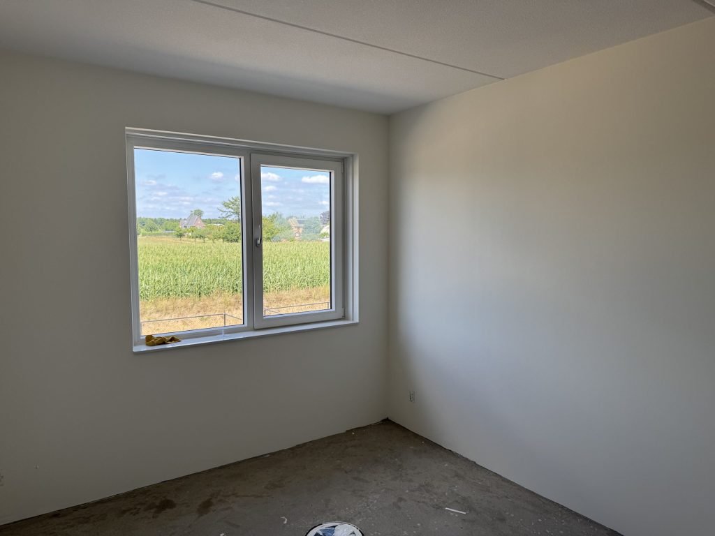 Lege nieuwbouwkamer met gladde, lichte wanden en een raam met uitzicht op een veld