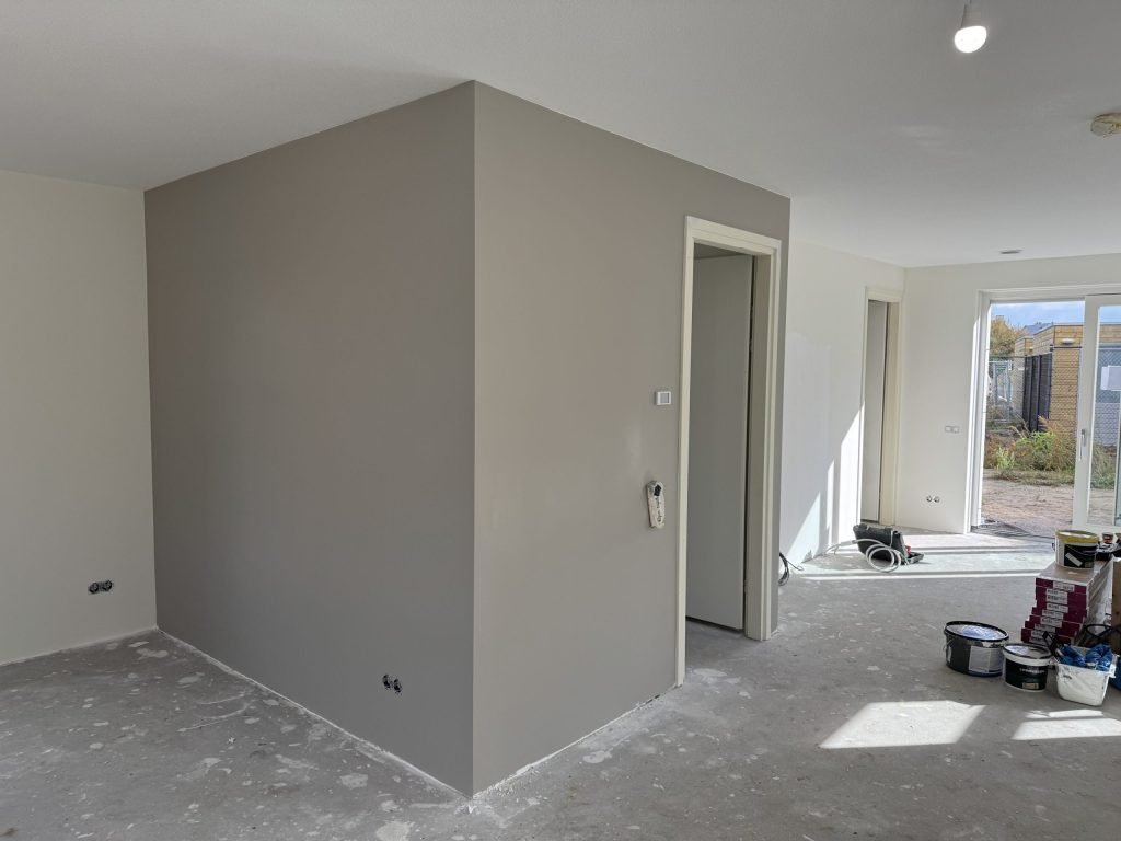 Pas gesausde grijze wand rond een trapkast, met verfemmers op de vloer
