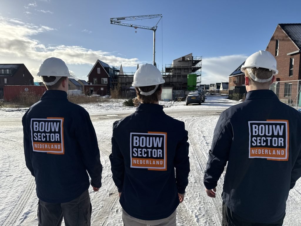 Drie vakmensen van Bouwsector Nederland met witte helm op een besneeuwde nieuwbouwlocatie